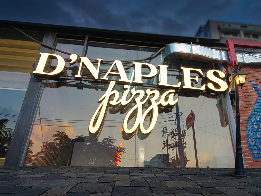 Cream 3D channel letters reading D'Naples pizza mounted above a glass shopfront at dusk