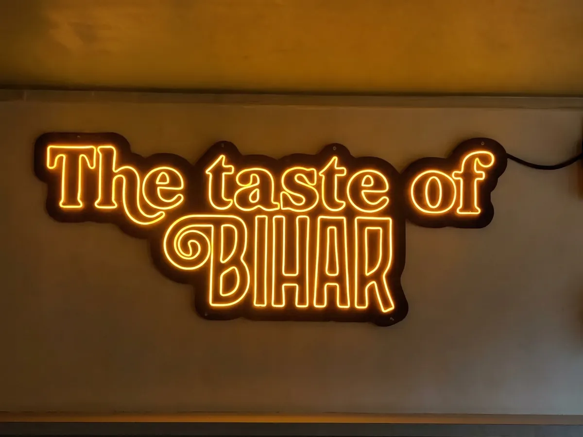 Warm orange LED neon sign reading The taste of Bihar glowing on a wall at night